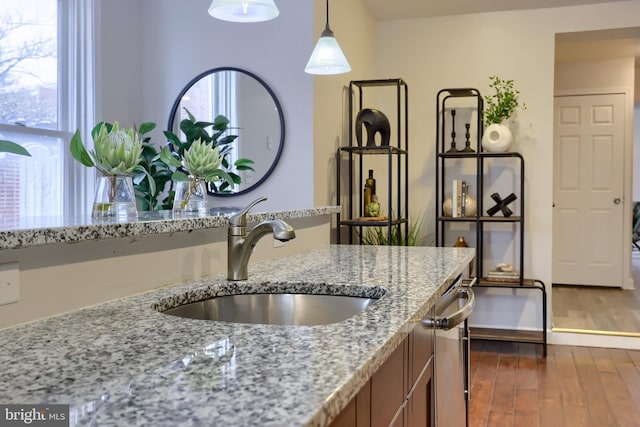 kitchen with a healthy amount of sunlight, light stone counters, pendant lighting, and a sink