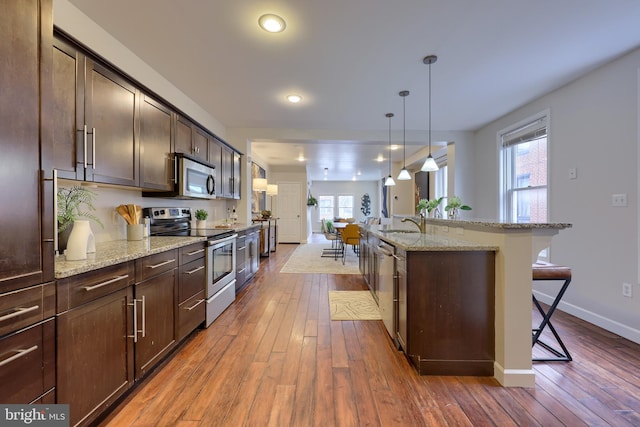 kitchen with light stone counters, a breakfast bar area, appliances with stainless steel finishes, an island with sink, and pendant lighting