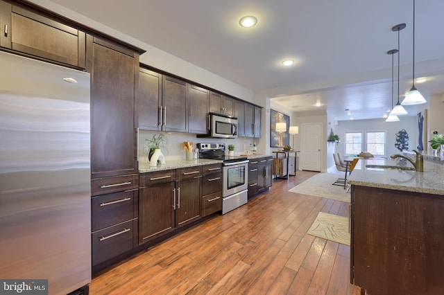 kitchen with dark brown cabinetry, appliances with stainless steel finishes, light stone counters, hanging light fixtures, and a sink