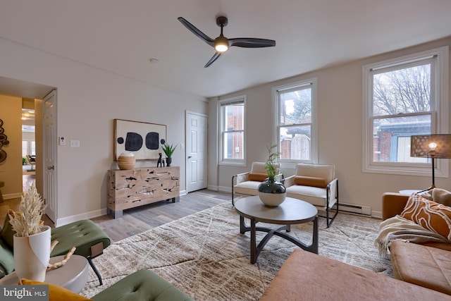 living area featuring a baseboard heating unit, baseboards, ceiling fan, and light wood finished floors