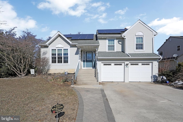 split level home with driveway, an attached garage, roof mounted solar panels, and roof with shingles