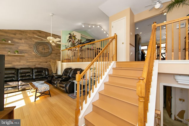 stairs with lofted ceiling, ceiling fan, wooden walls, and wood finished floors