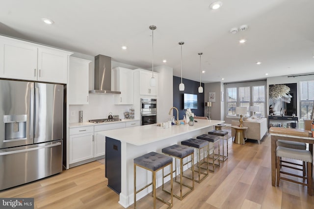 kitchen with light wood finished floors, wall chimney exhaust hood, a kitchen breakfast bar, stainless steel appliances, and a sink