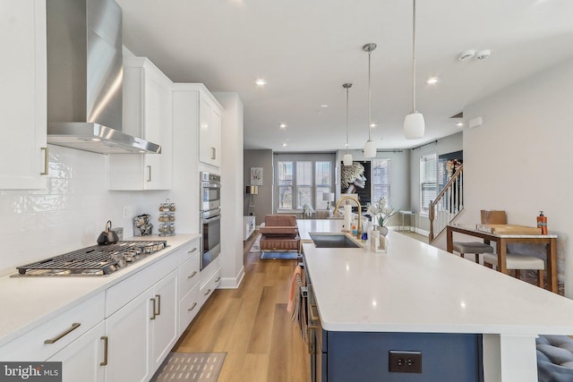 kitchen with stainless steel appliances, a sink, backsplash, wall chimney exhaust hood, and light wood finished floors