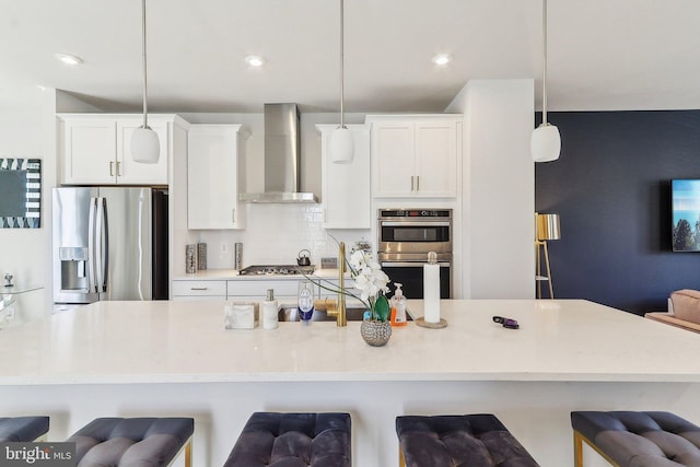 kitchen with a breakfast bar, stainless steel appliances, decorative backsplash, white cabinetry, and wall chimney exhaust hood