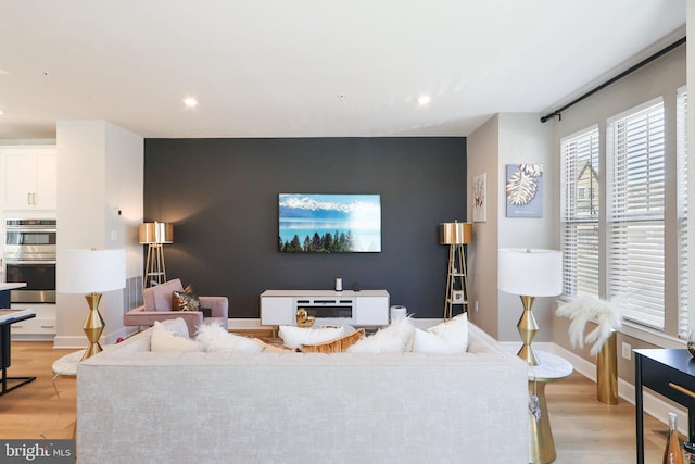 living room with light wood-type flooring, an accent wall, baseboards, and recessed lighting