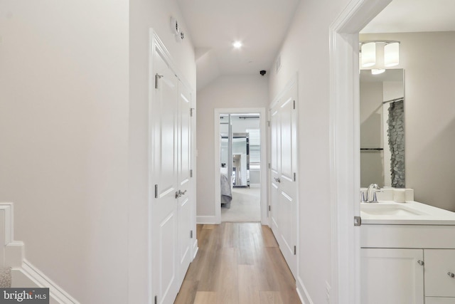 corridor with a sink, light wood-style flooring, and baseboards