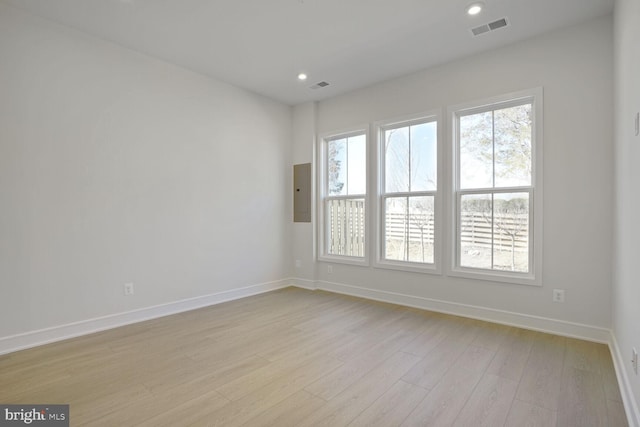 empty room with electric panel, baseboards, visible vents, light wood-style floors, and recessed lighting