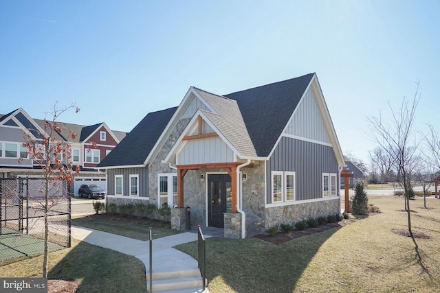 view of front facade featuring stone siding, a front lawn, board and batten siding, and roof with shingles