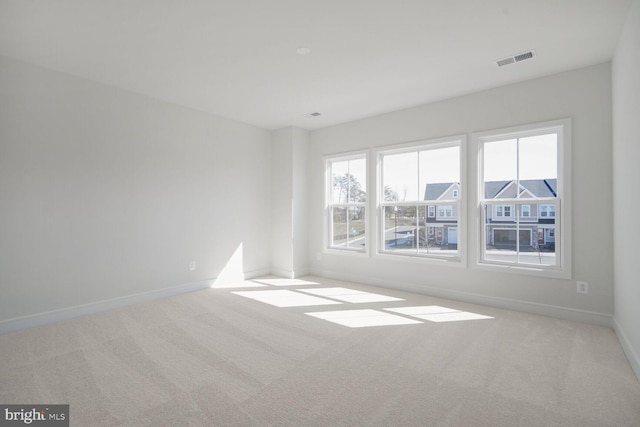 spare room with light colored carpet, visible vents, and baseboards