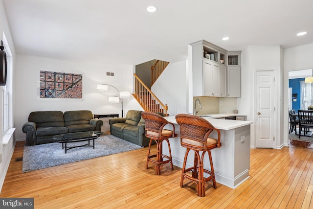 living area featuring baseboards, visible vents, stairway, light wood-type flooring, and recessed lighting