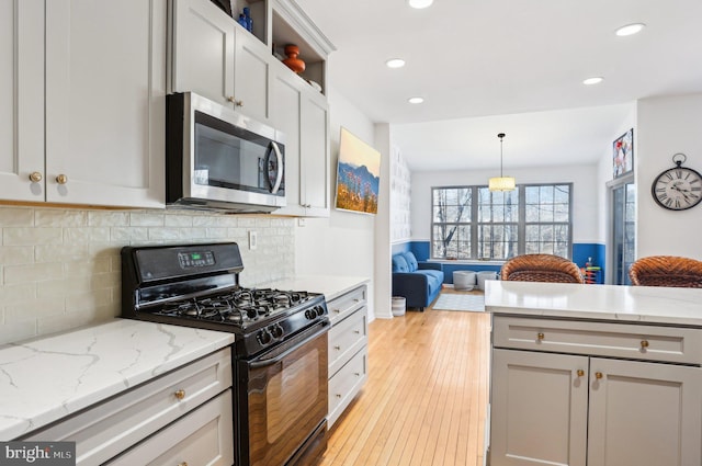 kitchen featuring light wood finished floors, tasteful backsplash, black gas range oven, stainless steel microwave, and open floor plan