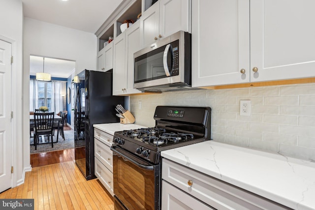 kitchen featuring open shelves, light stone countertops, black appliances, light wood finished floors, and tasteful backsplash