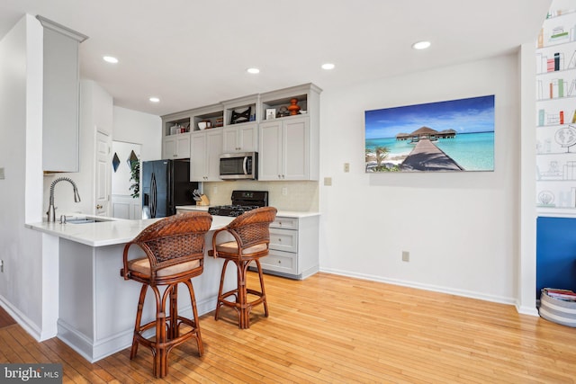 kitchen with light wood-style floors, a breakfast bar, light countertops, black appliances, and a sink