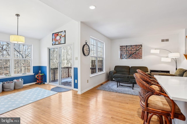 living room featuring plenty of natural light, wood-type flooring, lofted ceiling, and visible vents