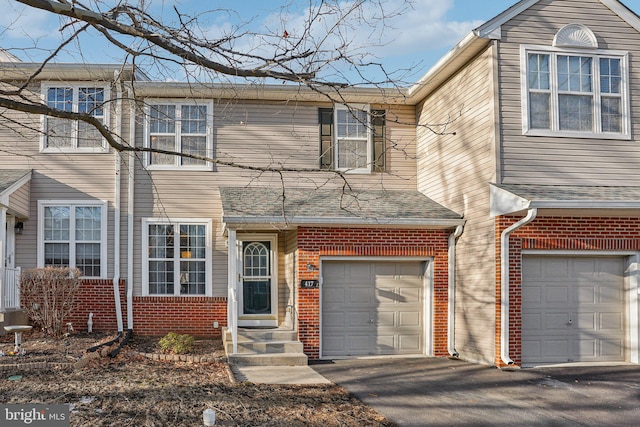 view of front facade featuring a garage, driveway, brick siding, and a shingled roof