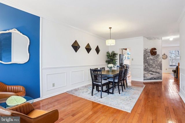 dining room featuring wood-type flooring, wainscoting, crown molding, and a decorative wall