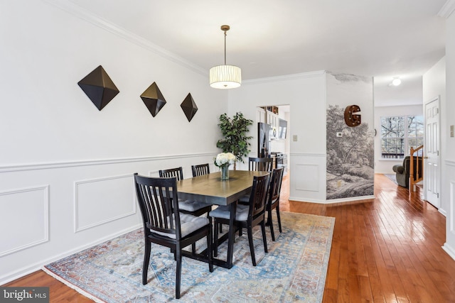 dining space featuring hardwood / wood-style flooring, a wainscoted wall, stairway, ornamental molding, and a decorative wall