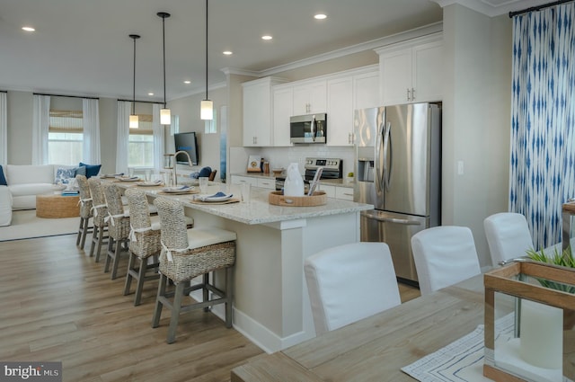 kitchen with stainless steel appliances, light stone counters, a center island with sink, and white cabinets