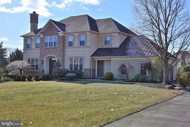 view of front of home featuring a chimney, stucco siding, a front yard, a standing seam roof, and metal roof