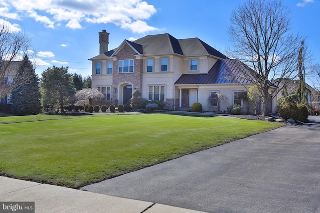 view of front of house with a standing seam roof, metal roof, a chimney, and a front lawn