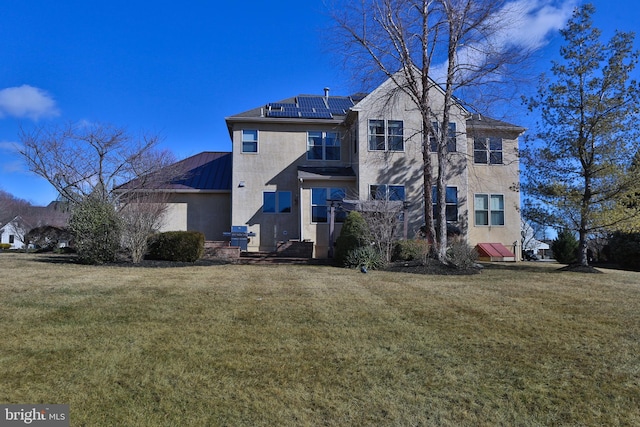 back of house with roof mounted solar panels, metal roof, a lawn, and stucco siding