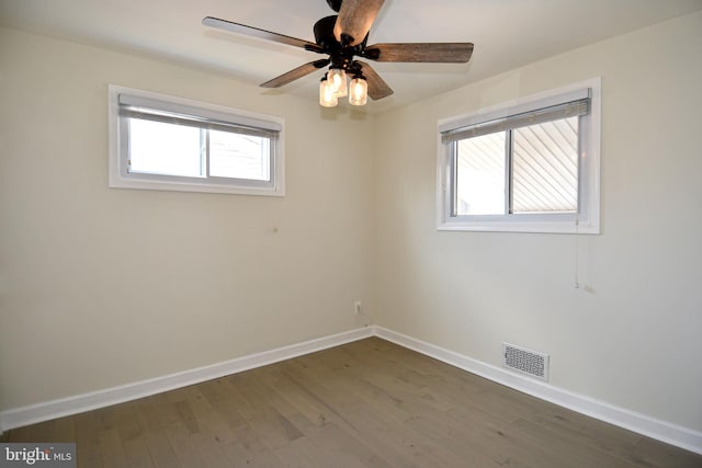 spare room with dark wood-style floors, baseboards, visible vents, and a wealth of natural light