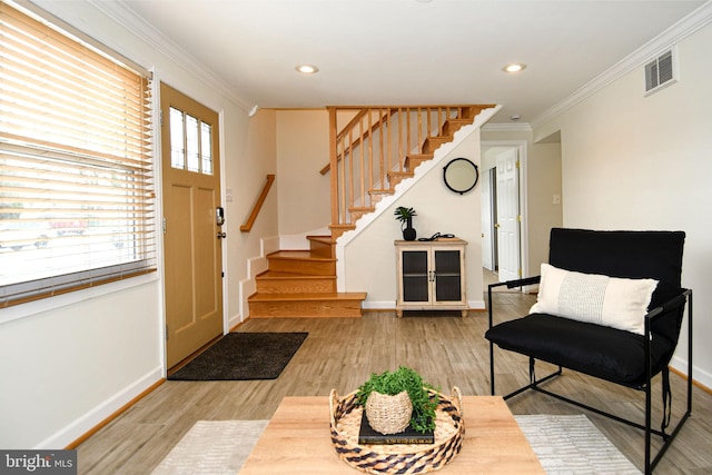 foyer entrance with baseboards, visible vents, ornamental molding, wood finished floors, and stairs