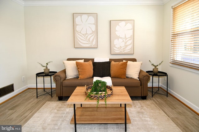 living room featuring ornamental molding, baseboards, visible vents, and light wood finished floors