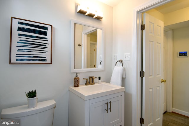 half bath featuring toilet, wood finished floors, vanity, and baseboards