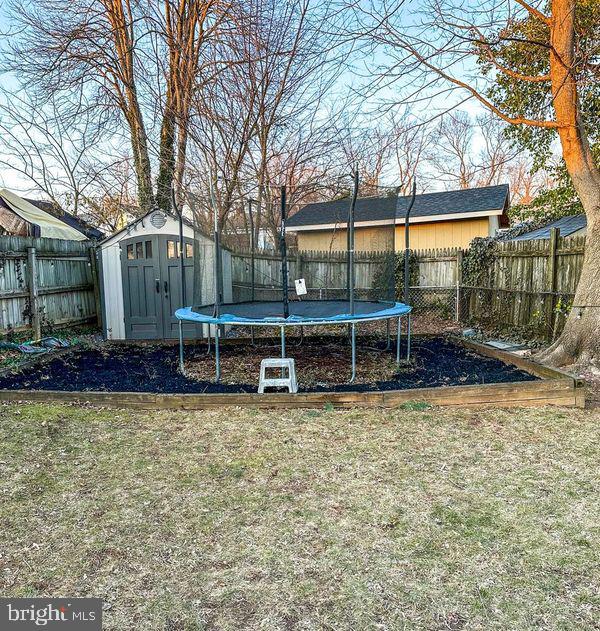 view of yard featuring a trampoline, a fenced backyard, an outdoor structure, and a storage shed