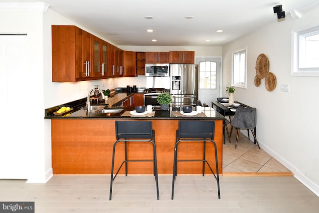 kitchen with dark countertops, glass insert cabinets, a breakfast bar, a peninsula, and stainless steel appliances