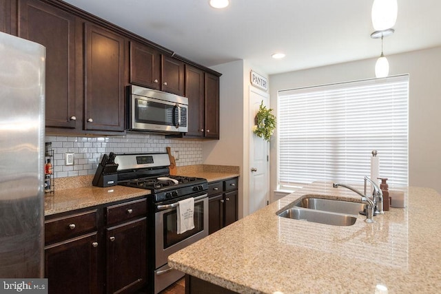 kitchen with dark brown cabinetry, a sink, hanging light fixtures, appliances with stainless steel finishes, and tasteful backsplash