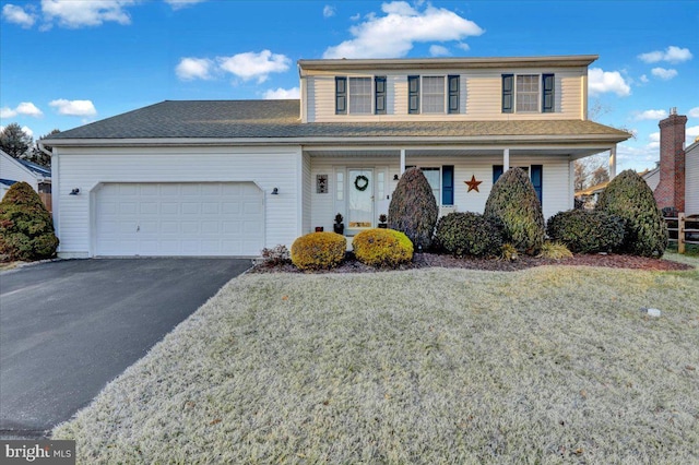 traditional home featuring a garage, covered porch, a front lawn, and aphalt driveway