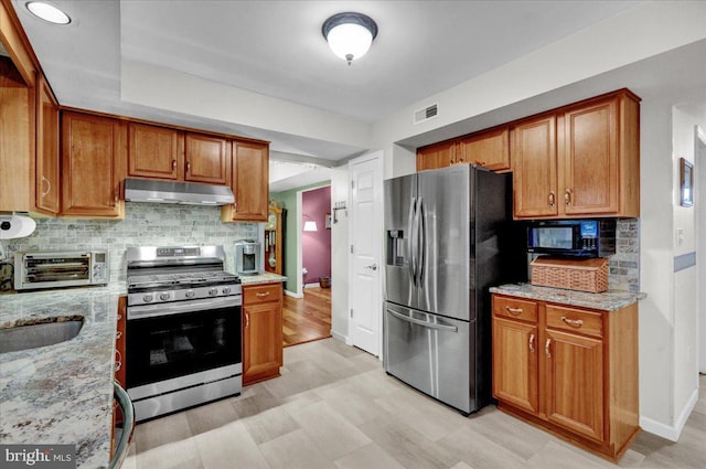 kitchen featuring light stone counters, a toaster, under cabinet range hood, stainless steel appliances, and decorative backsplash