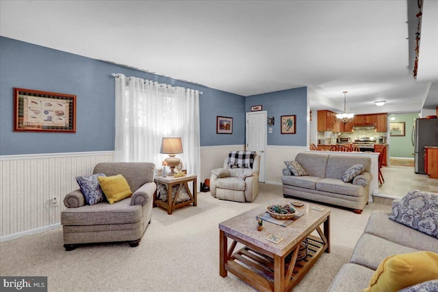 living area featuring light carpet, a wainscoted wall, and a chandelier