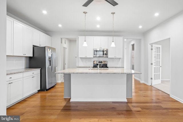 kitchen with appliances with stainless steel finishes, white cabinets, light wood-style floors, and backsplash