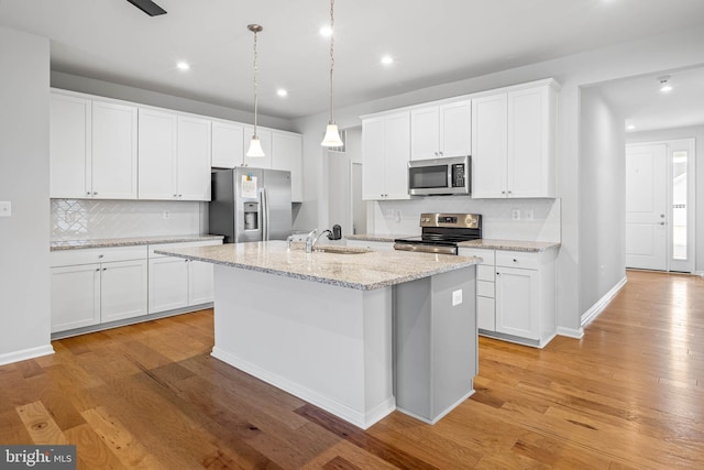 kitchen featuring stainless steel appliances, white cabinets, light wood-type flooring, a center island with sink, and decorative light fixtures