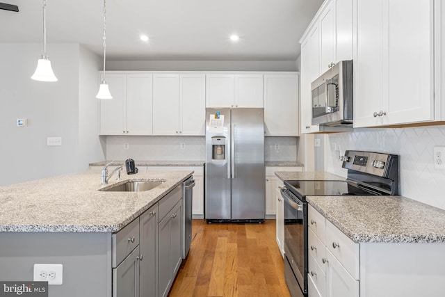 kitchen with gray cabinetry, stainless steel appliances, a sink, white cabinetry, and light wood finished floors