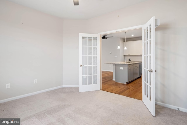 carpeted empty room with french doors, a sink, a ceiling fan, and baseboards