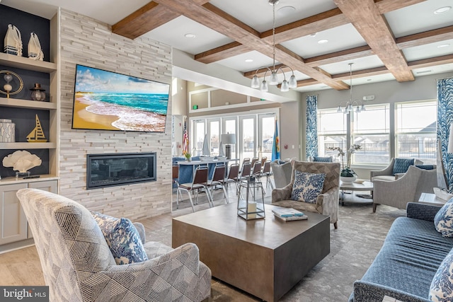 living room with a stone fireplace, built in shelves, a notable chandelier, coffered ceiling, and beamed ceiling