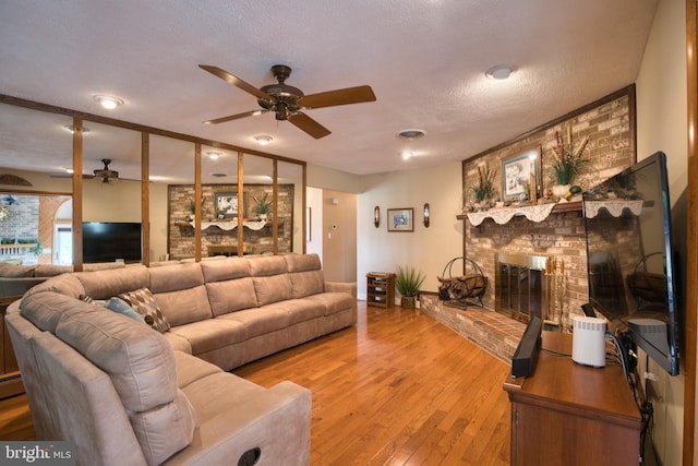 living room with a fireplace, visible vents, ceiling fan, a textured ceiling, and light wood-type flooring