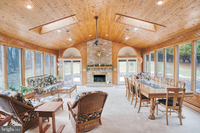 sunroom / solarium featuring wooden ceiling, vaulted ceiling with skylight, a fireplace, and a ceiling fan