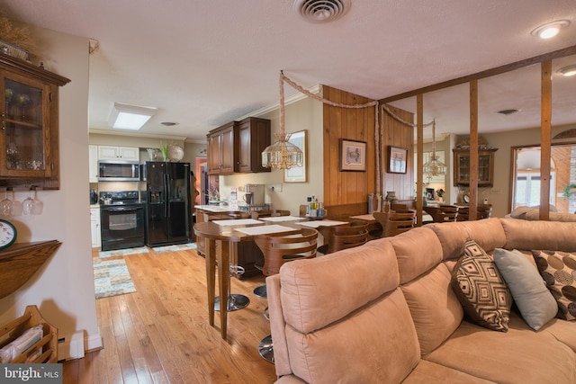 living room with a baseboard heating unit, ornamental molding, light wood-type flooring, and visible vents