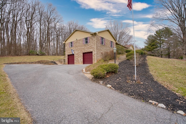 view of front of home featuring aphalt driveway, a front yard, brick siding, and a garage