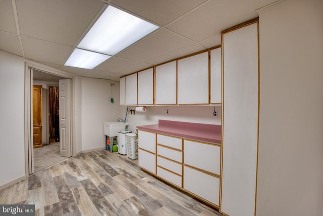 basement featuring baseboards, a drop ceiling, a sink, and light wood finished floors