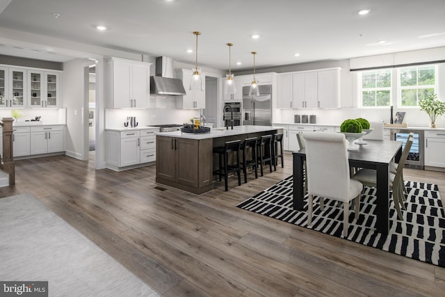 kitchen with an island with sink, wall chimney exhaust hood, decorative light fixtures, built in refrigerator, and light countertops