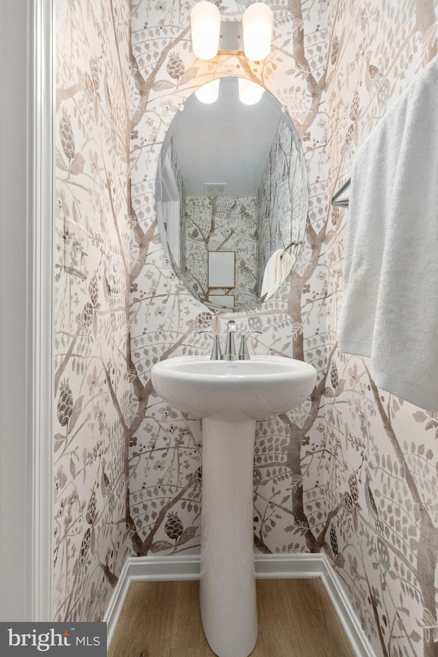 bathroom with wood finished floors, baseboards, and wallpapered walls