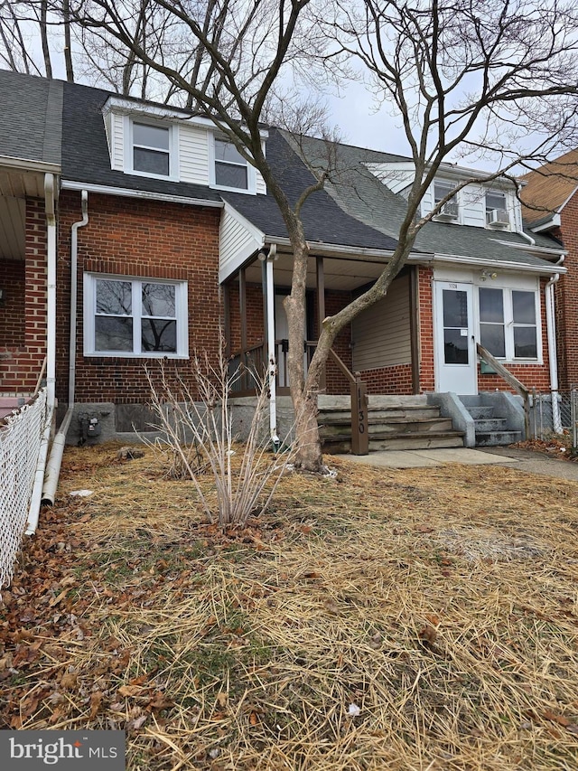 view of front of property with a shingled roof, entry steps, brick siding, and fence