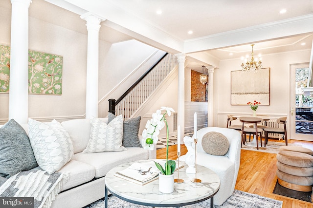 living area featuring a notable chandelier, crown molding, stairway, wood finished floors, and ornate columns